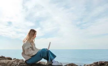 Workation - eine Frau sitzt mit Laptop am Meer