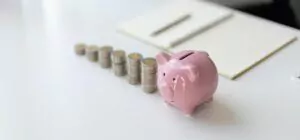 Auf einem Tisch steht ein rosa Sparschwein daneben gestapelte Euromünzen