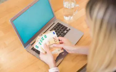 Frau sitz vor ihrem Laptop und zählt Euroscheine